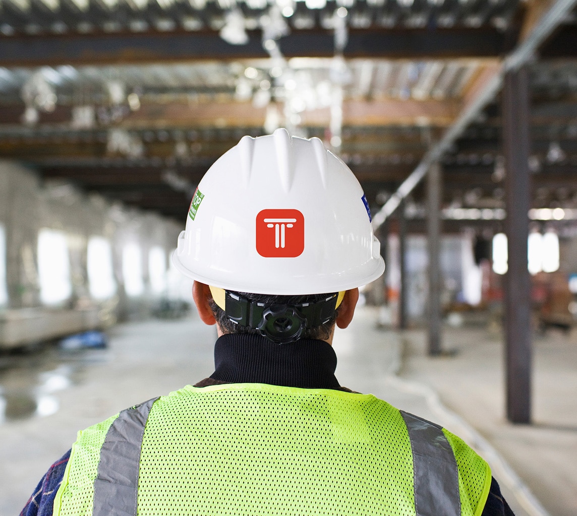 A construction worker wearing a white helmet and a reflective vest stands in an unfinished building interior under construction.