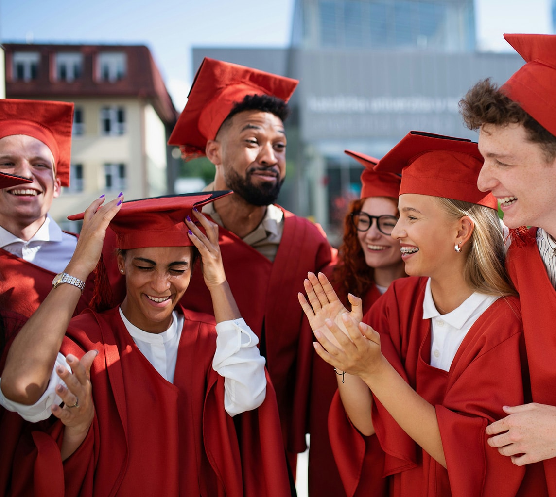 A group of joyful graduates in red caps and gowns celebrate together outdoors.