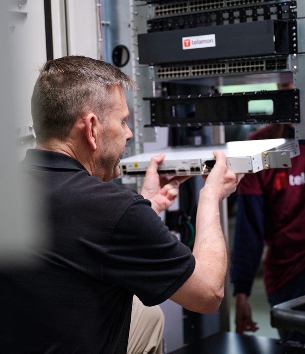 A man is installing a component in a server rack, with the Telamon logo visible in the background.