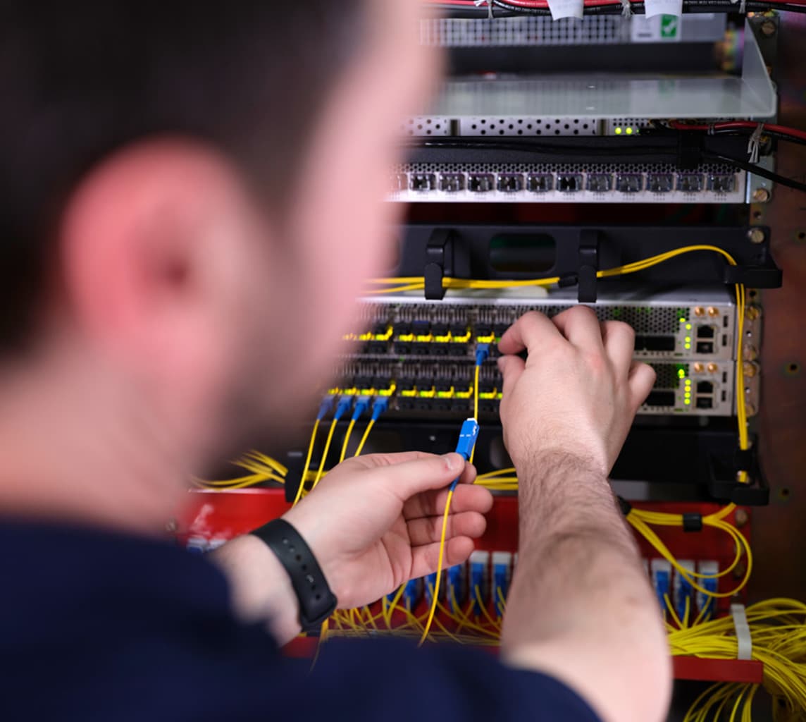 A person connects wires to a rack-mounted network switch in a data center.