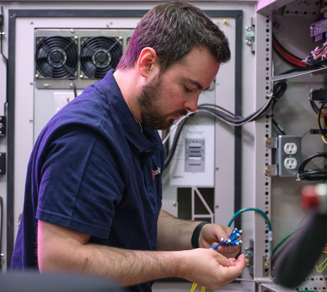 A person in a blue shirt is inspecting and arranging wires inside an open electrical panel with various components.