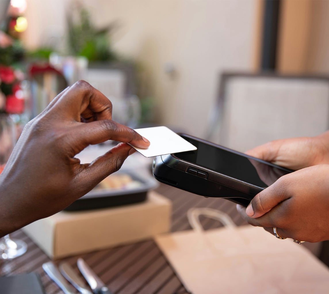 Person making a contactless payment by tapping a card on a card reader held by another person.