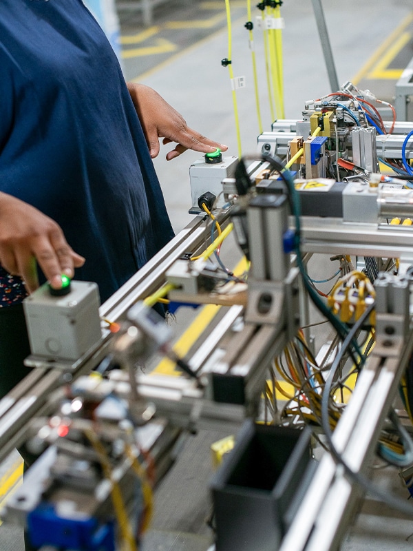 A person operating machinery in an industrial setting, pressing buttons on control panels connected to an intricate assembly of wires and mechanical components.