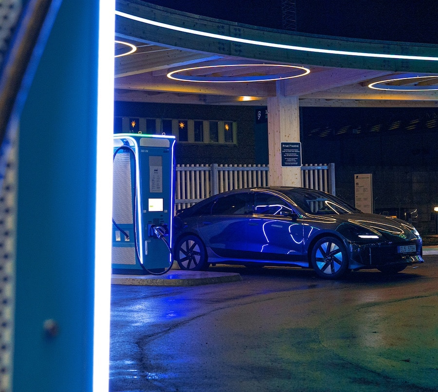 A sleek electric car charges at a futuristic, neon-lit charging station at night.